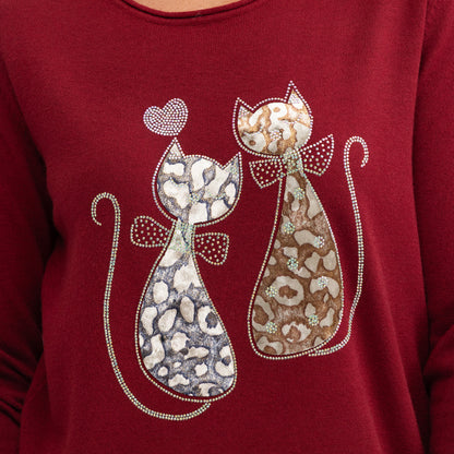 A close-up of a burgundy long-sleeve top featuring a decorative graphic of two stylized cats with leopard and cheetah-style spots, outlined with rhinestones, on the chest.