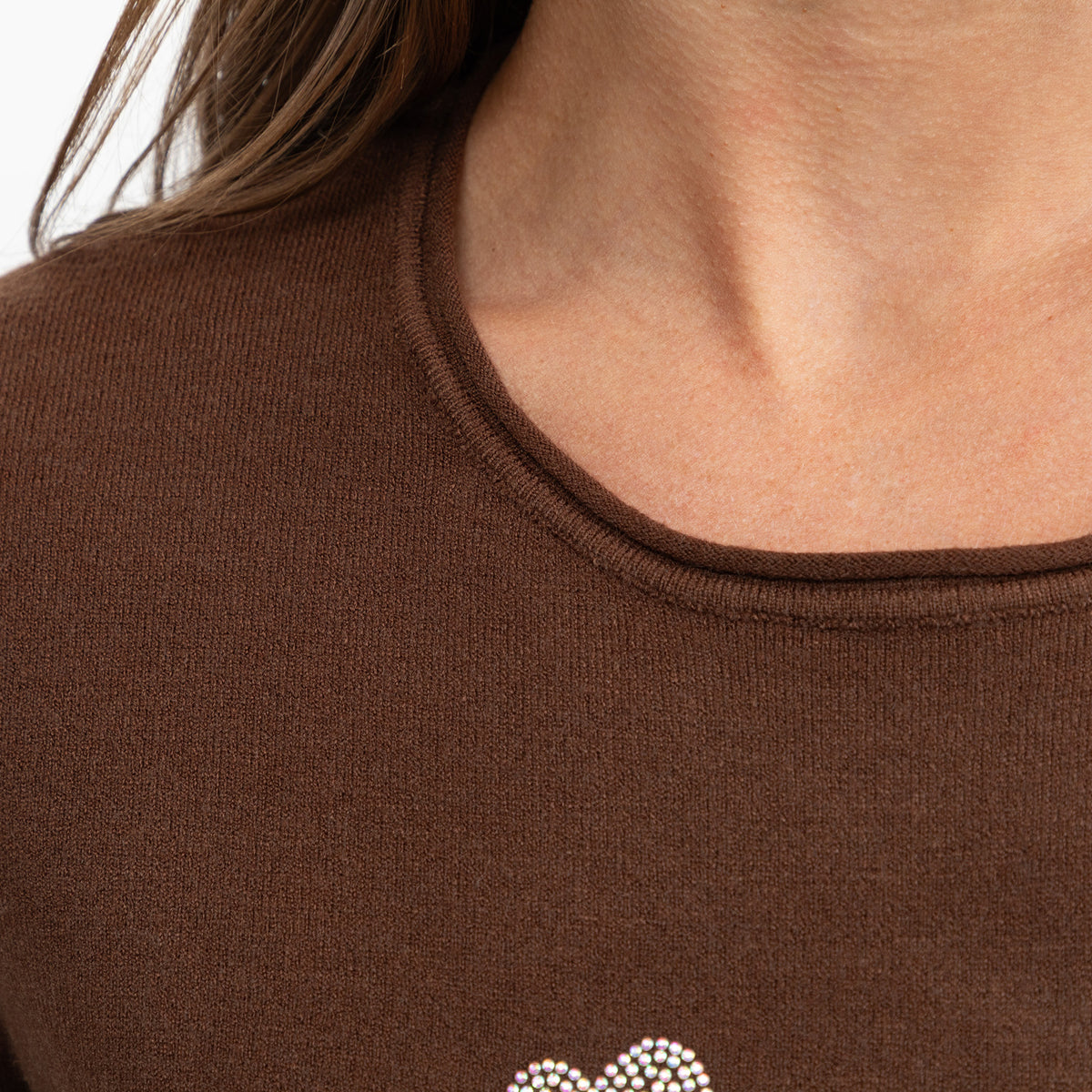 Close-up of a person wearing a brown ribbed knit top with a small rhinestone-embellished heart at the lower chest.