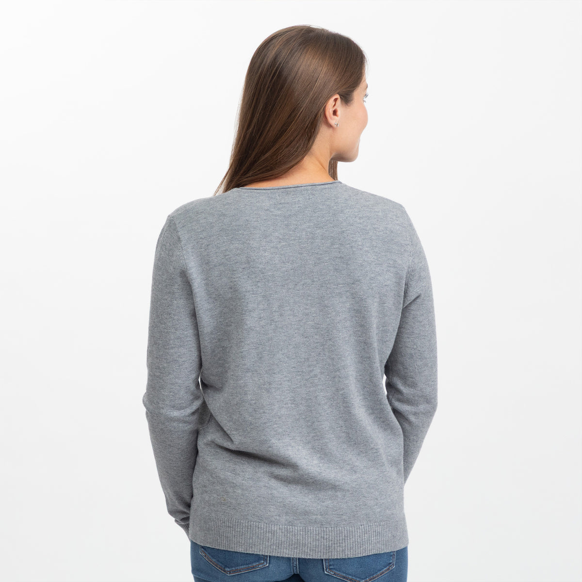 A woman viewed from the back wearing a light gray knit sweater and blue jeans against a plain white studio background.