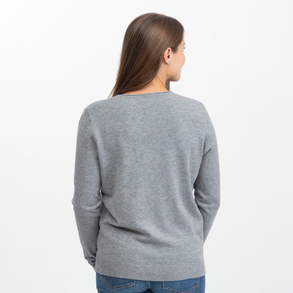 A woman viewed from the back wearing a light gray knit sweater and blue jeans against a plain white studio background.