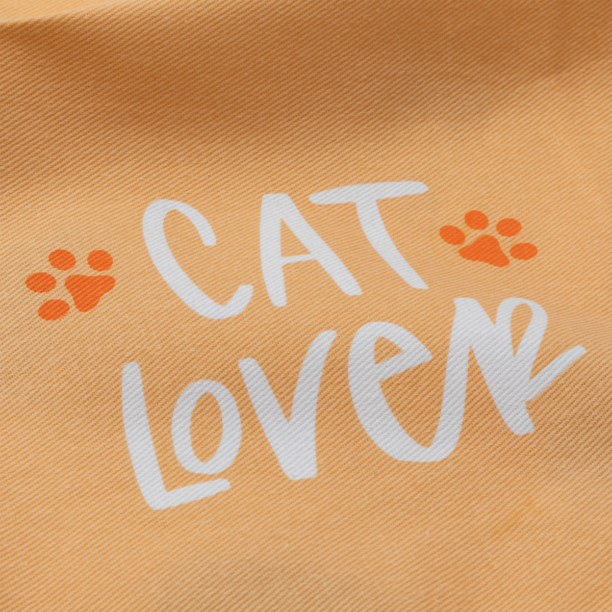 A close-up of a peach-colored fabric with a printed design that reads 'CAT LOVER' in white script, accented by two orange paw prints.