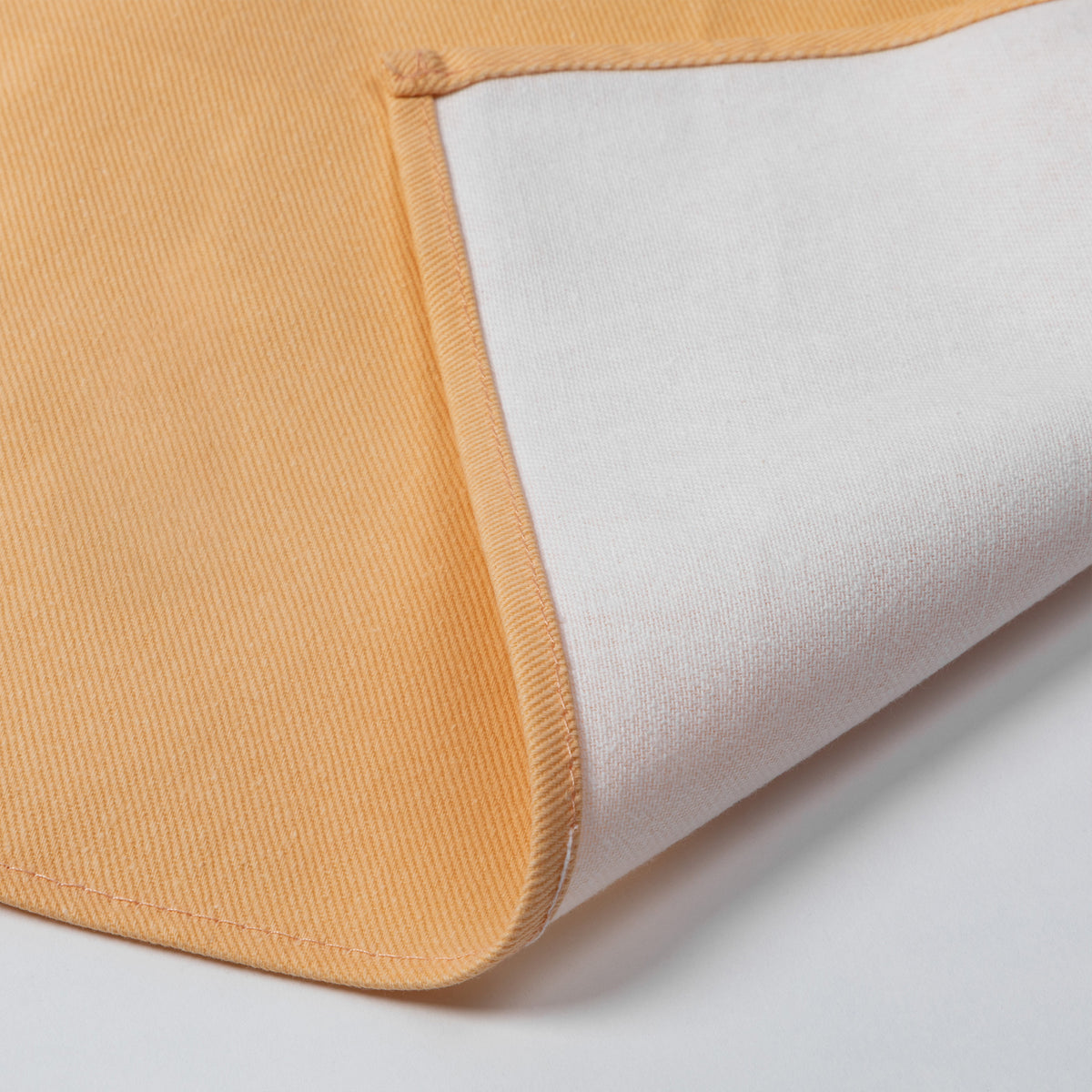 Close-up of a folded textile product showing a mustard yellow fabric side and a white backing, photographed on a clean white background.