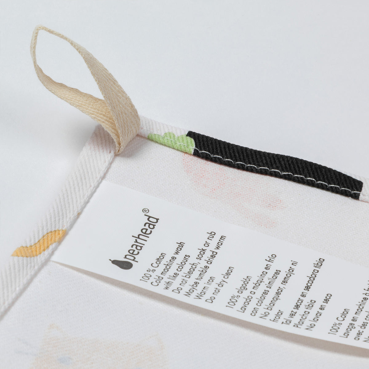 Close-up of a white Pearhead cotton dish towel with a beige hanging loop, a black stitched trim, and a printed care label.