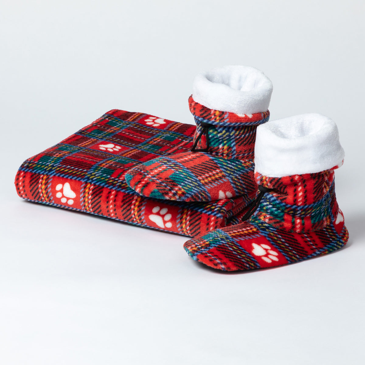 A matching pet bootie set including a folded plaid blanket and two slipper boots, all in a red tartan pattern with white paw prints and white fleece lining, on a light gray background.
