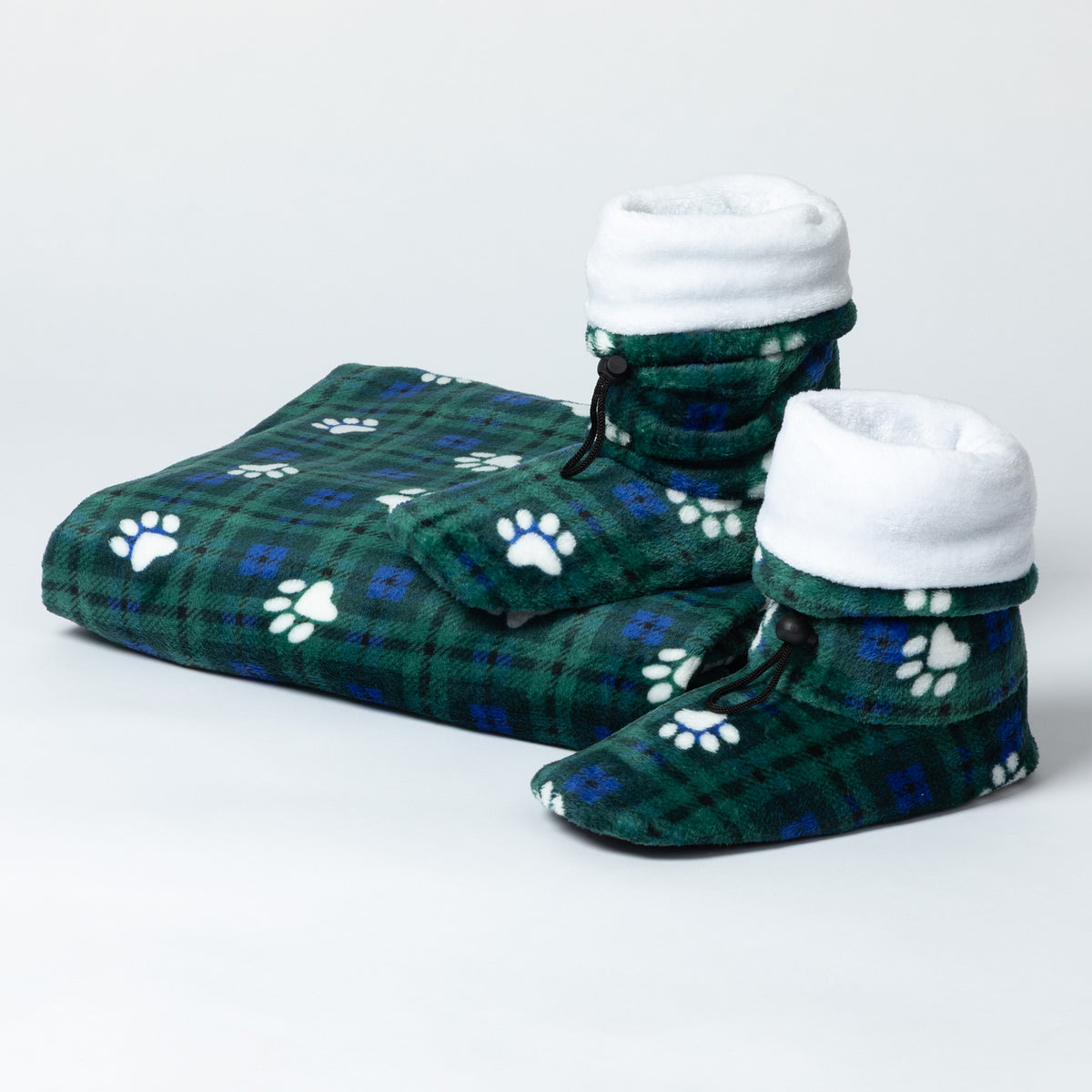 A pair of plush pet slippers and a matching folded blanket in a green plaid pattern with white paw prints, photographed on a clean light gray studio background.
