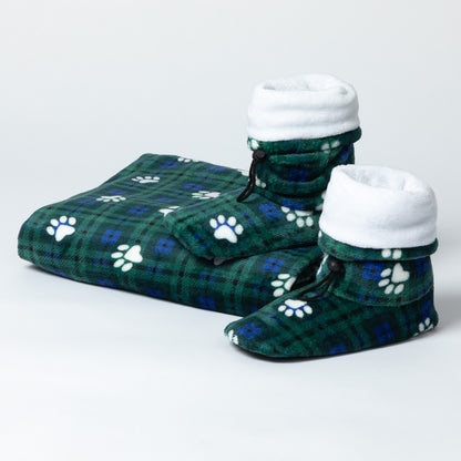 A pair of plush pet slippers and a matching folded blanket in a green plaid pattern with white paw prints, photographed on a clean light gray studio background.