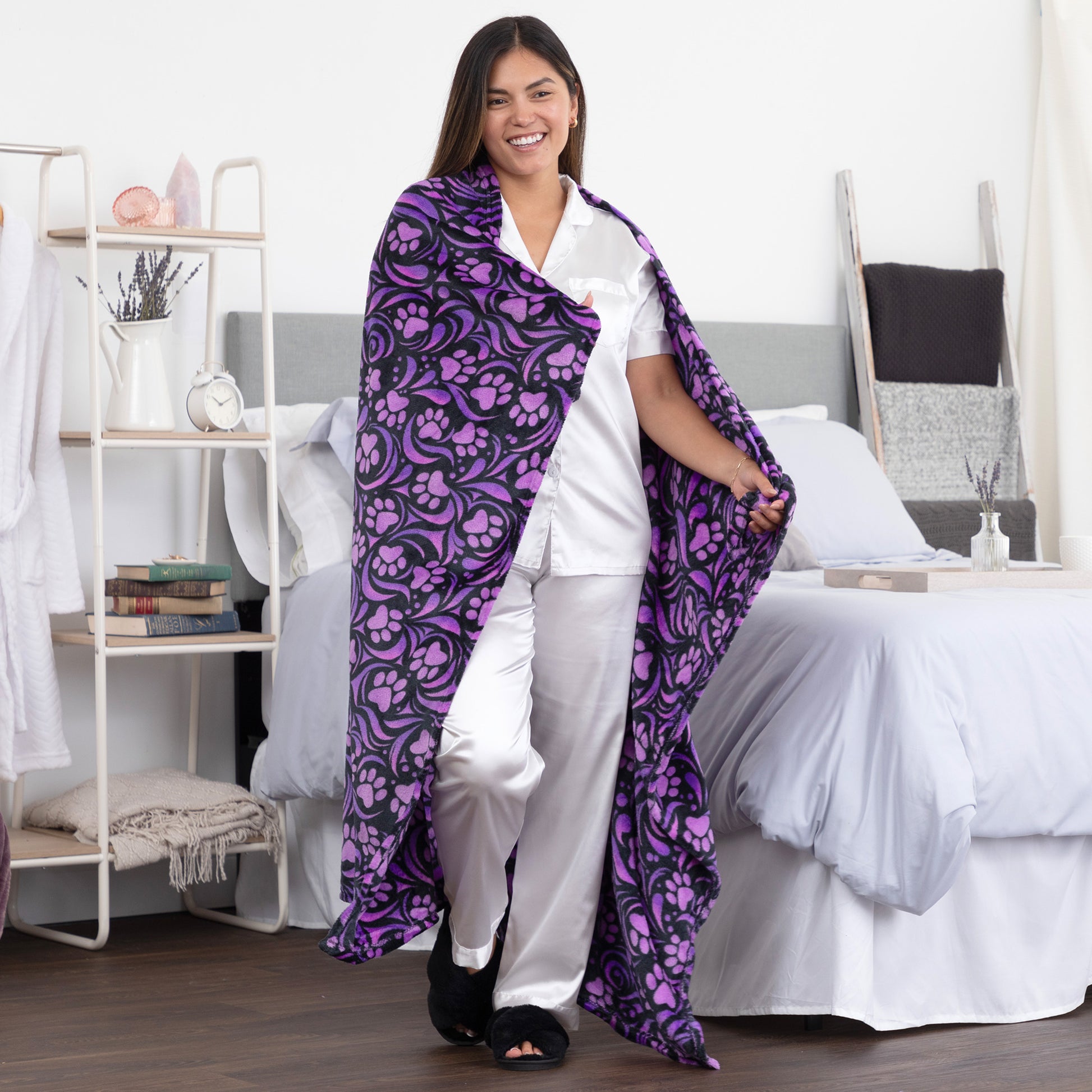 Woman holding a purple and black paw print blanket in a bedroom setting