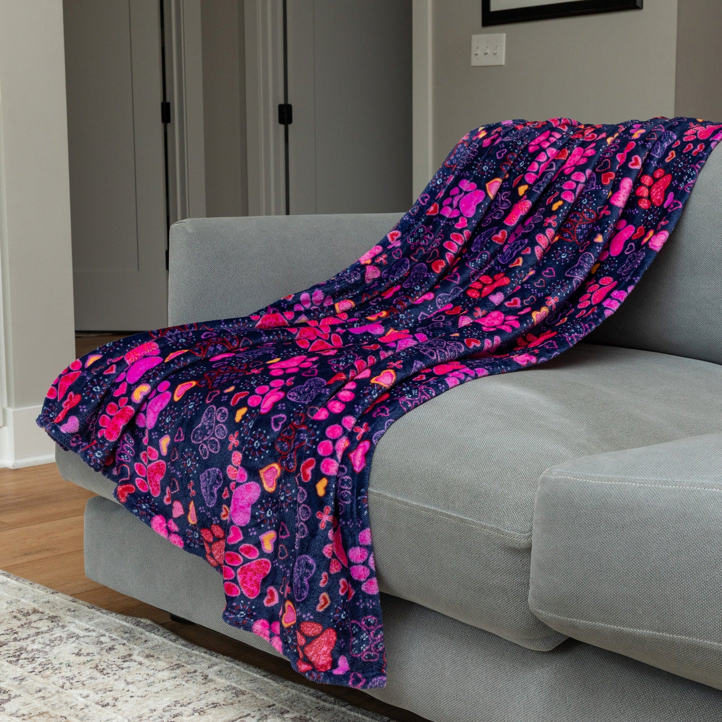 Colorful heart and paw print patterned blanket draped over a gray sofa in a living room.