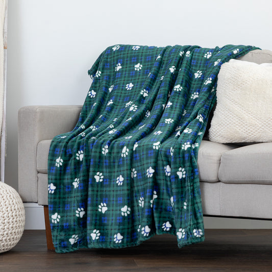 A green plaid throw blanket with white paw prints draped over a light gray sofa in a living room setting.