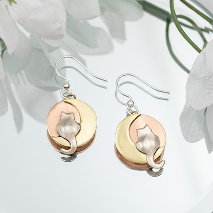 Pair of cat-themed earrings with brass, copper, and silver finish on a light background