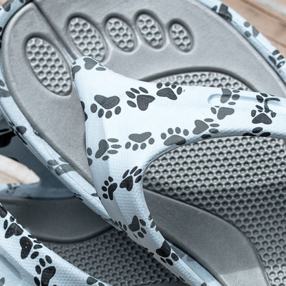 White sandals with black paw print designs on the straps, with a textured insole.