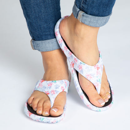 A pair of waves and marble paws print design EVA flip flops on a person's feet standing indoors on a white background, the waves and marble paws print is on white background and the textured foot bed is black