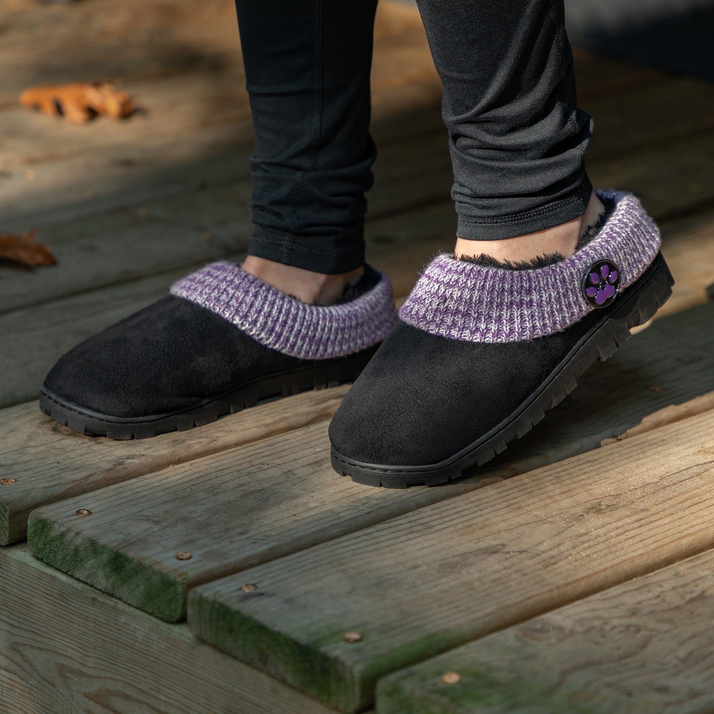 Black slippers with purple accents and black faux fur lining, on a wooden deck outdoors.