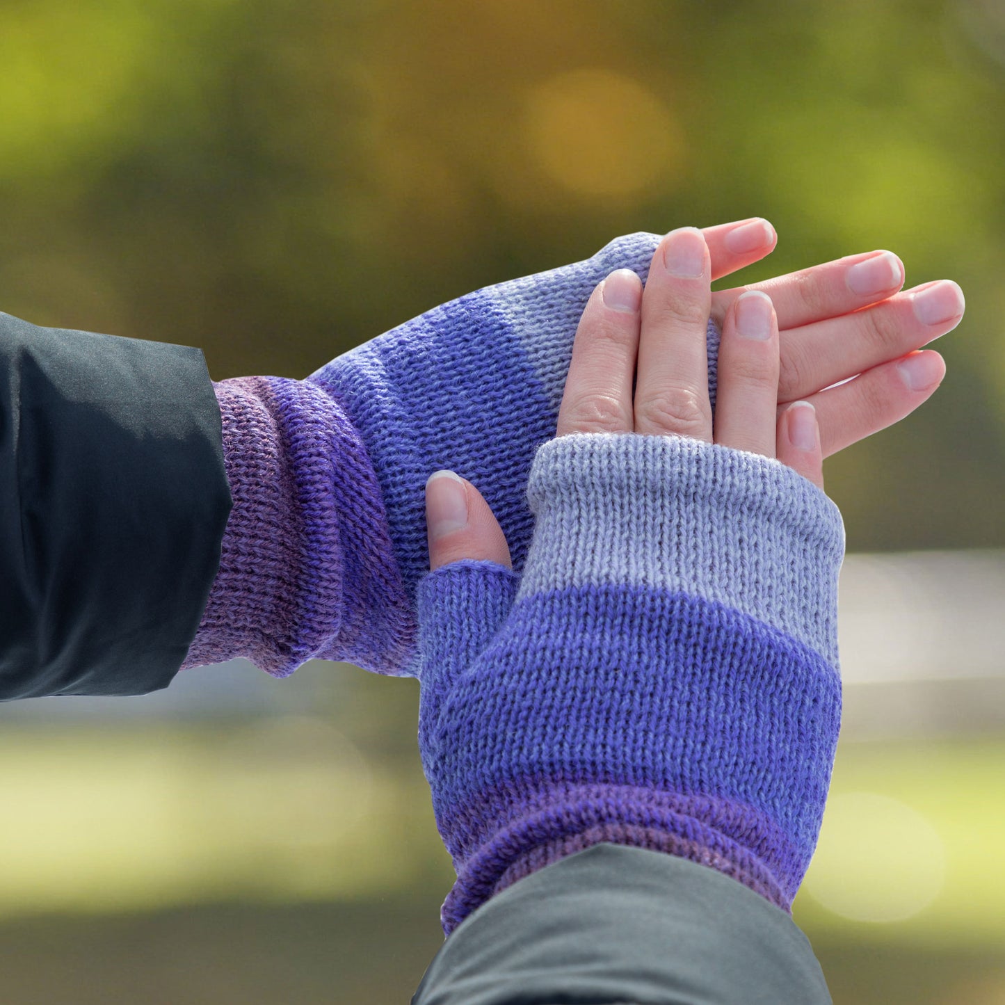 Close-up of hands wearing purple fingerless gloves against a blurred natural background