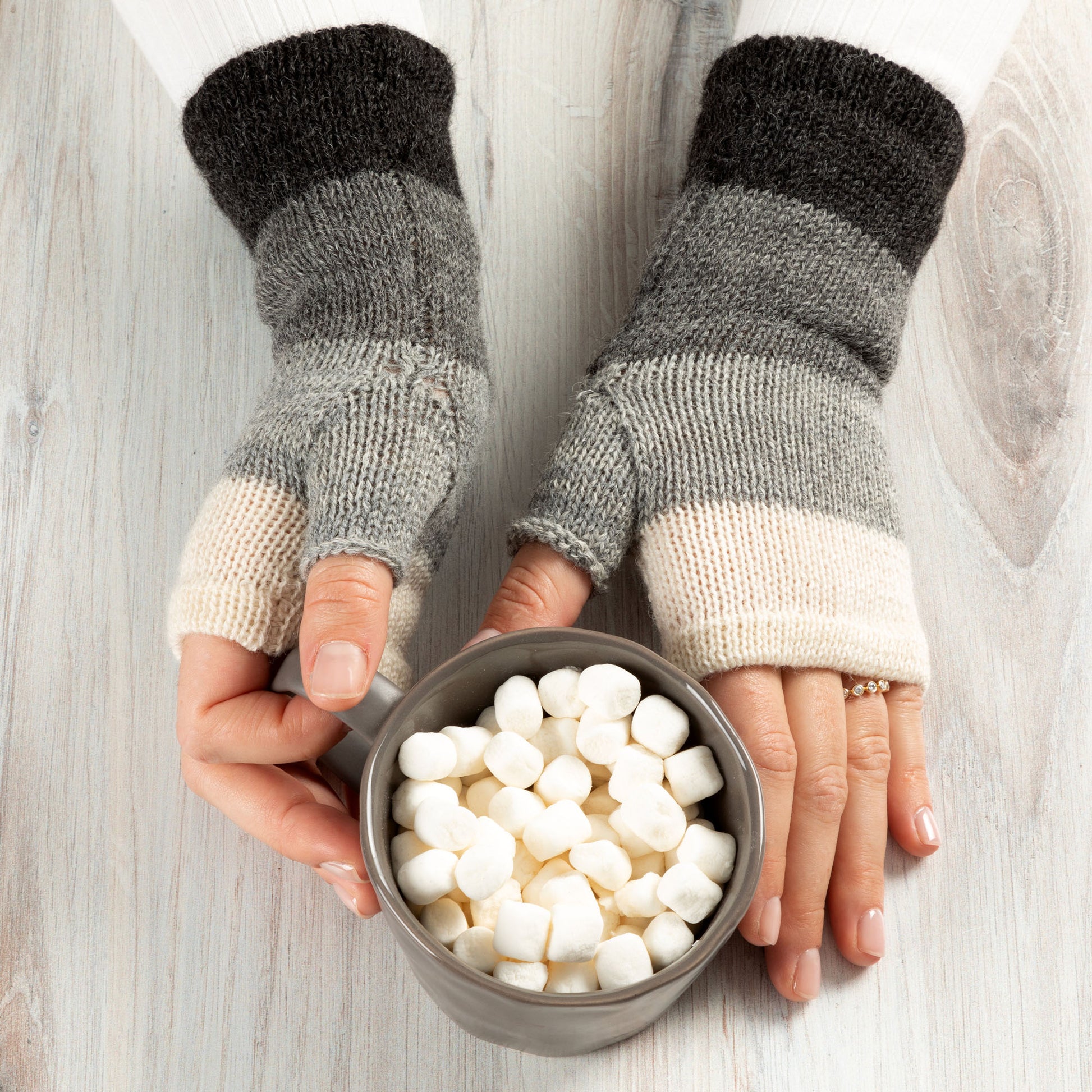 Person wearing fingerless gloves holding a bowl of marshmallows on a wooden surface