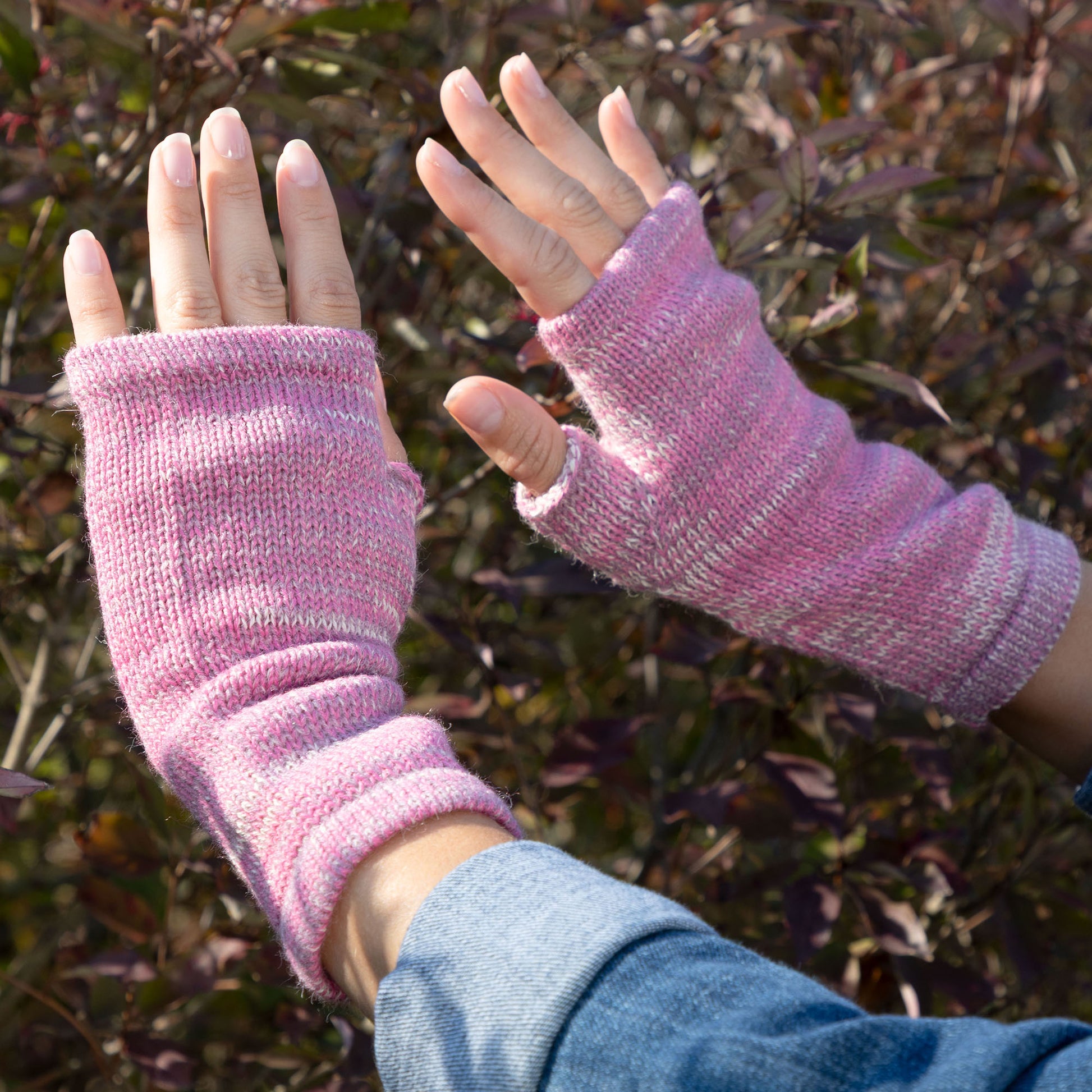 Pink knitted fingerless gloves worn outdoors with a blurred natural background