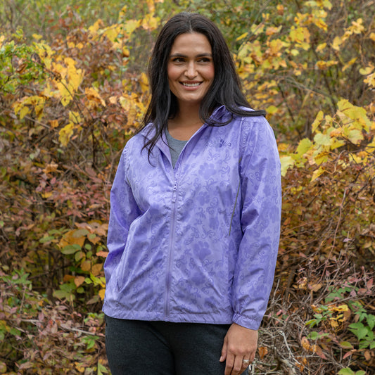 Woman wearing a purple rain jacket with a hidden paw pattern that activates when wet, while outside in the autumn leaves.