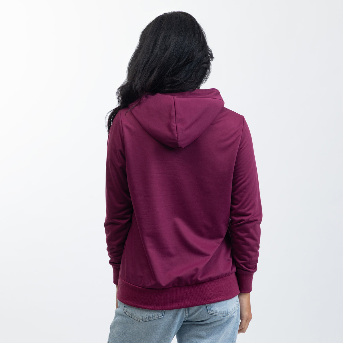 A woman viewed from behind wearing a deep burgundy hooded sweatshirt and light blue jeans against a plain white background.