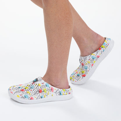 White slip-on shoes with colorful floral pattern worn by a person on a white background