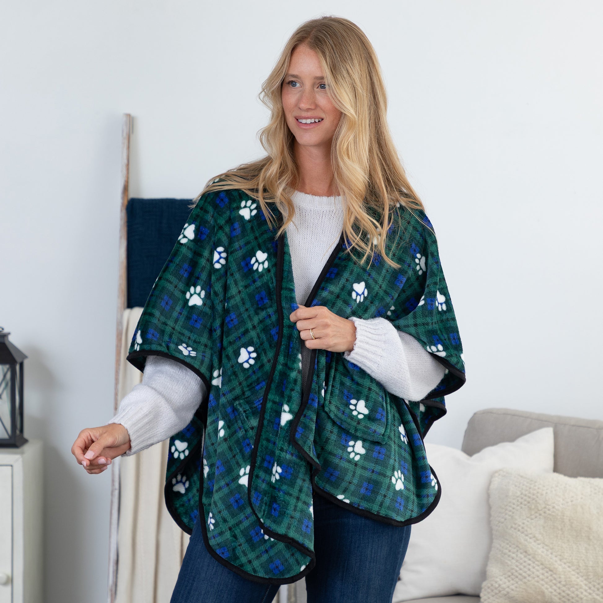 A woman wearing a green plaid poncho with white paw prints, standing in a living room setting.