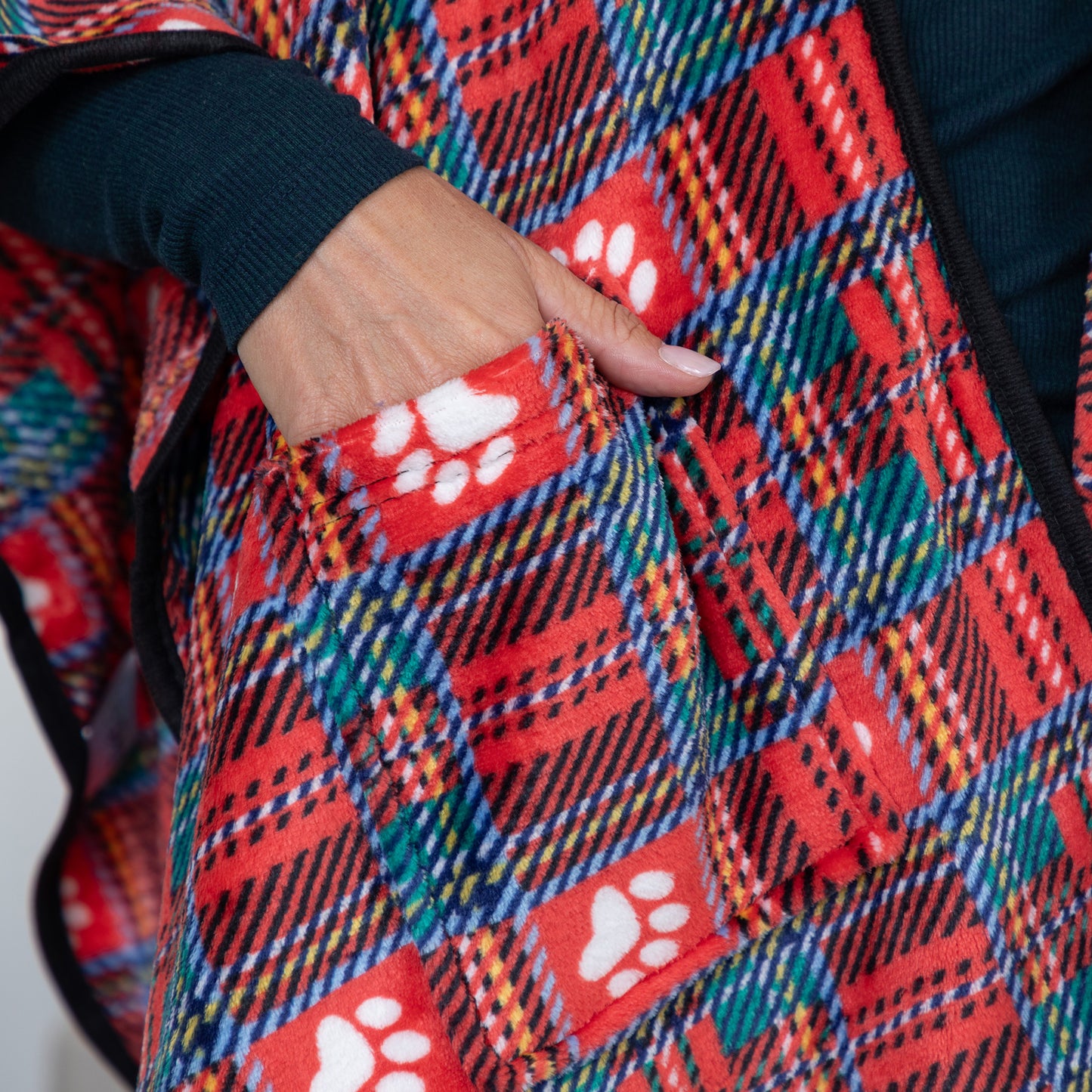 Close-up of a red plaid fleece vest with white paw print pockets, worn by a person whose hand is tucked into the pocket.