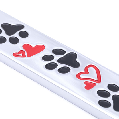 Close up of a license plate frame with black paw prints and red hearts on a white background