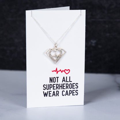 Necklace with heart pendant on a card with text 'Not all superheroes wear capes' against a dark background