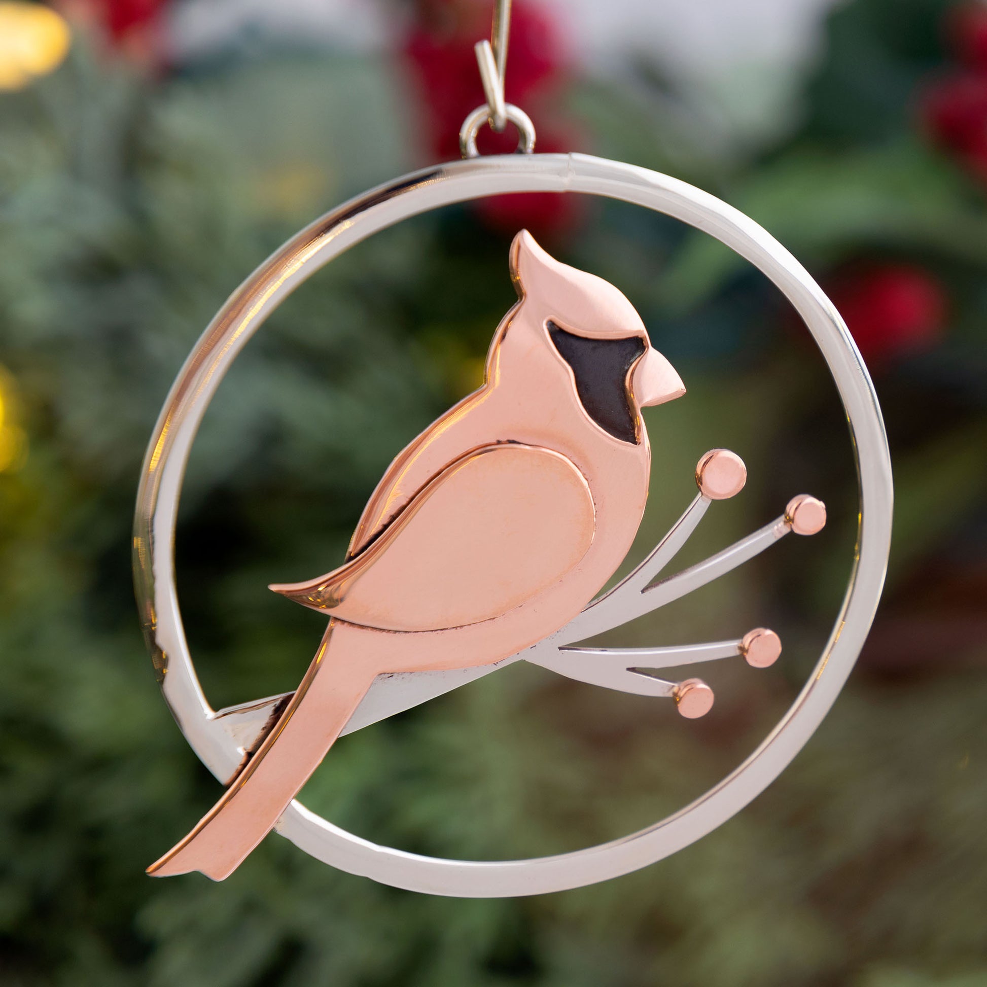 Copper cardinal bird ornament on a branch with a silver circular frame against a blurred green background.