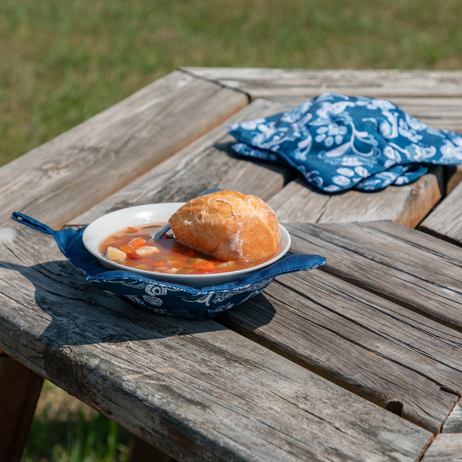 Bowl Cozy with warm soup and bread in an outdoor space, including a paw print design, blue paisley paws