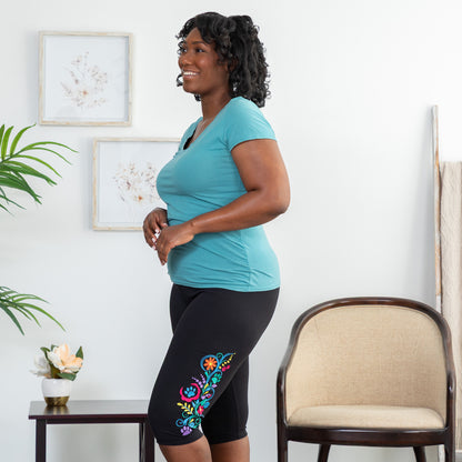 Woman wearing a turquoise top and black legging shorts with floral embroidery in a living room.