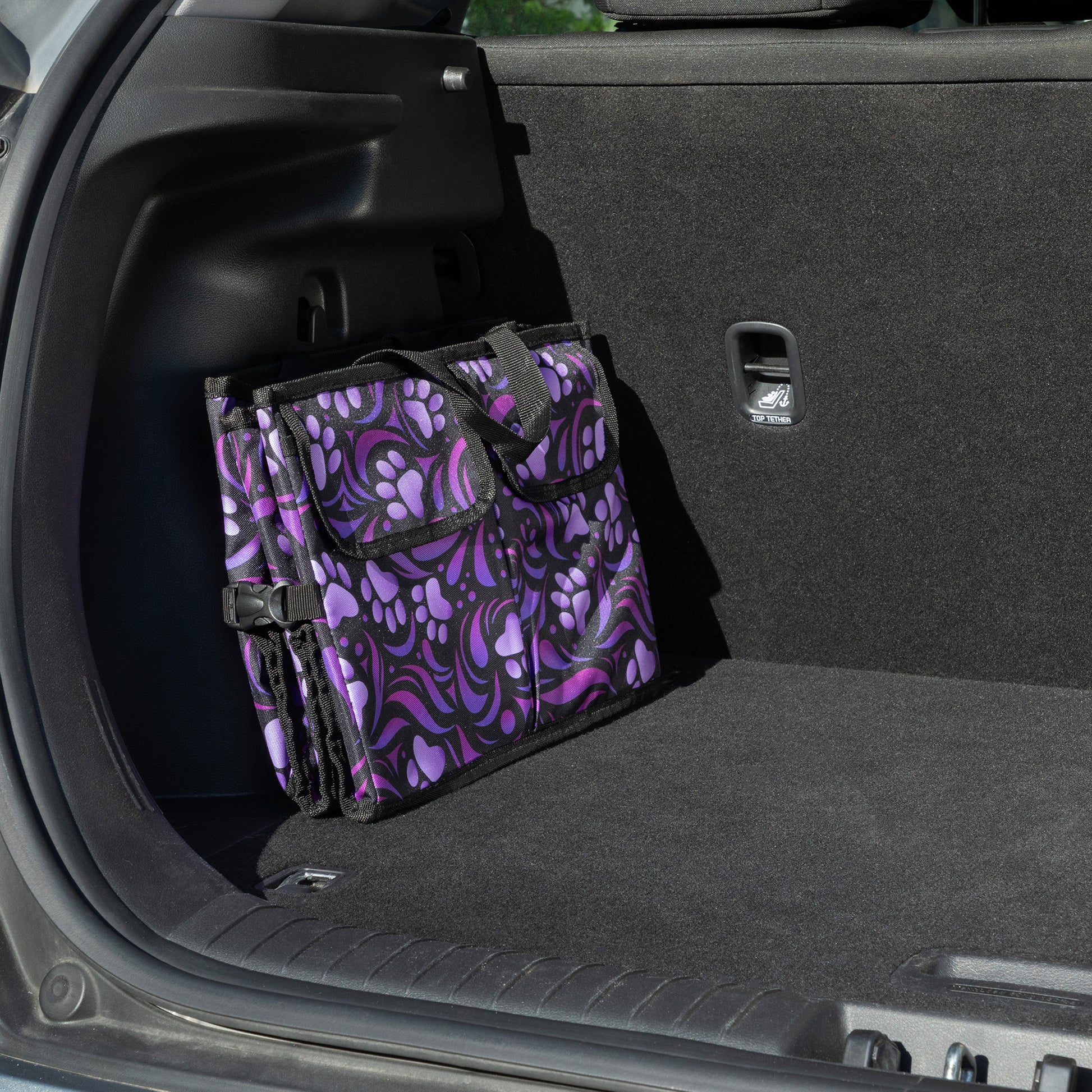 A purple paw print patterned car trunk organizer folded flat, in a car trunk.