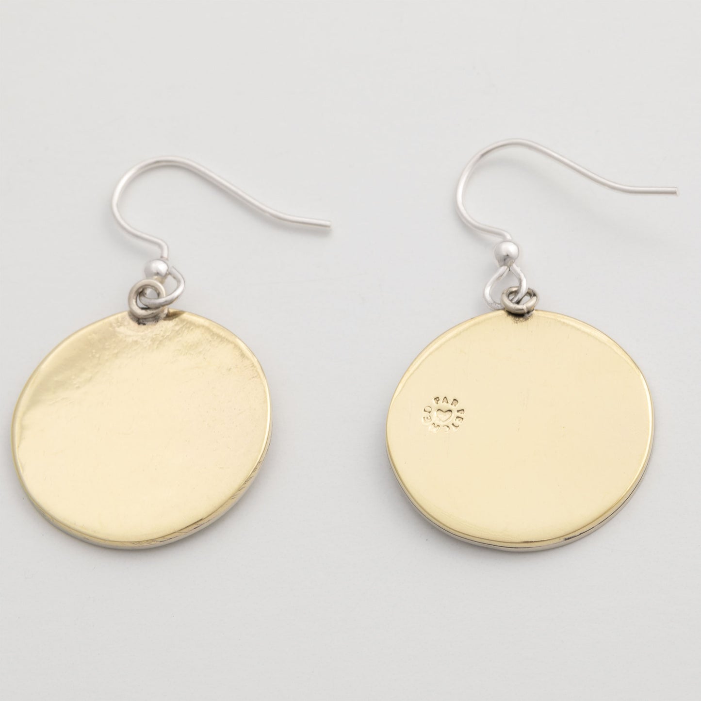The brass backside of round earrings on a light gray background