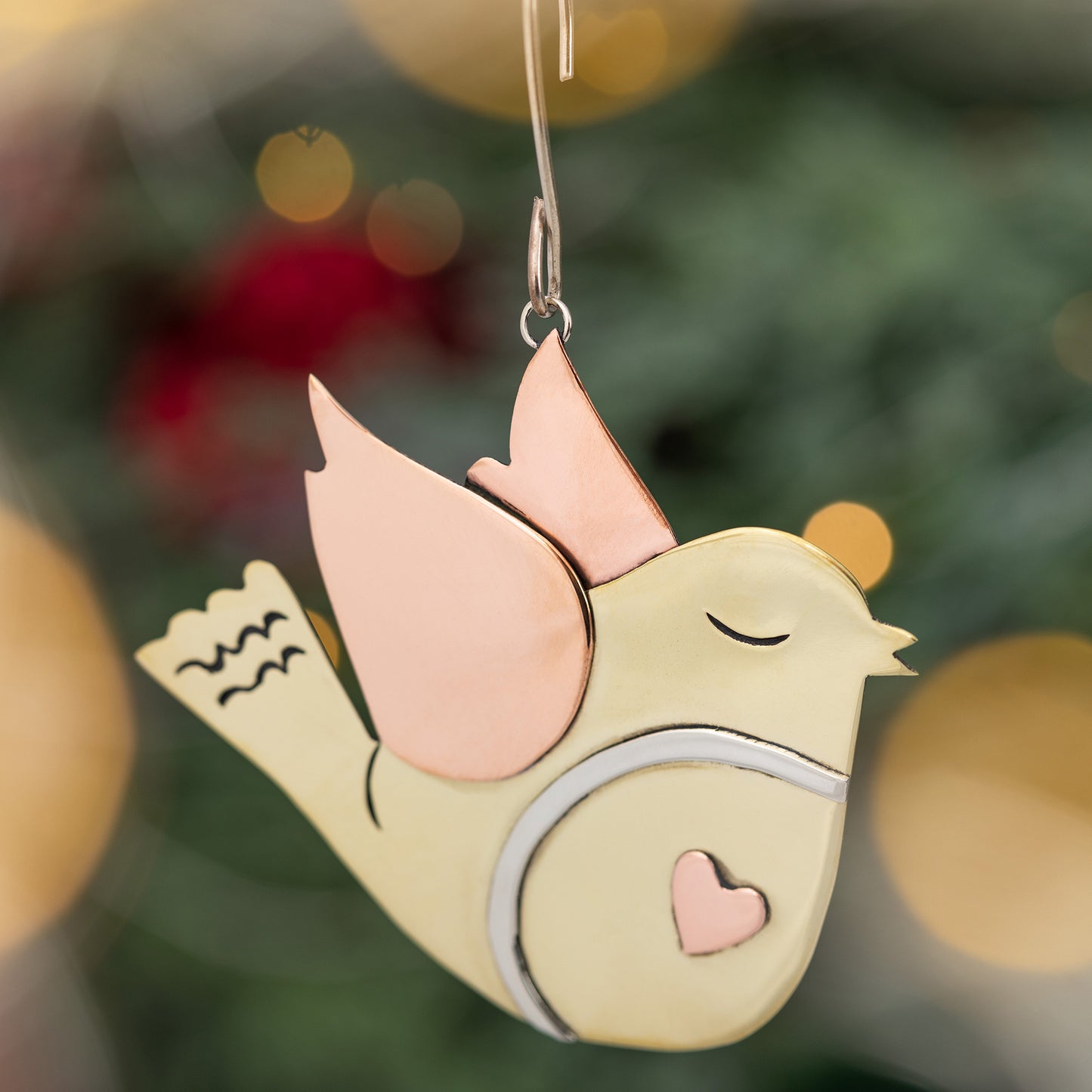 Decorative bird ornament with copper wings against a blurred Christmas tree background