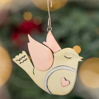 Decorative bird ornament with copper wings against a blurred Christmas tree background
