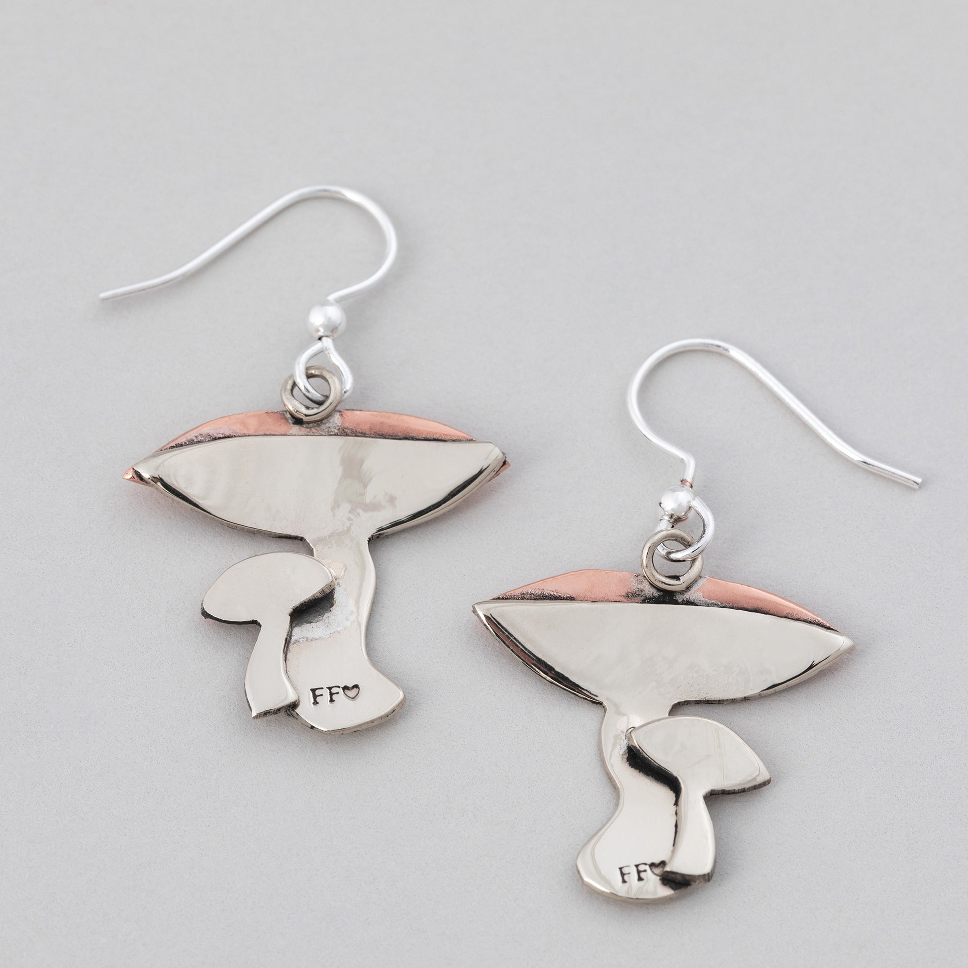 Mushroom-shaped earring backs with copper and silver on a gray background.
