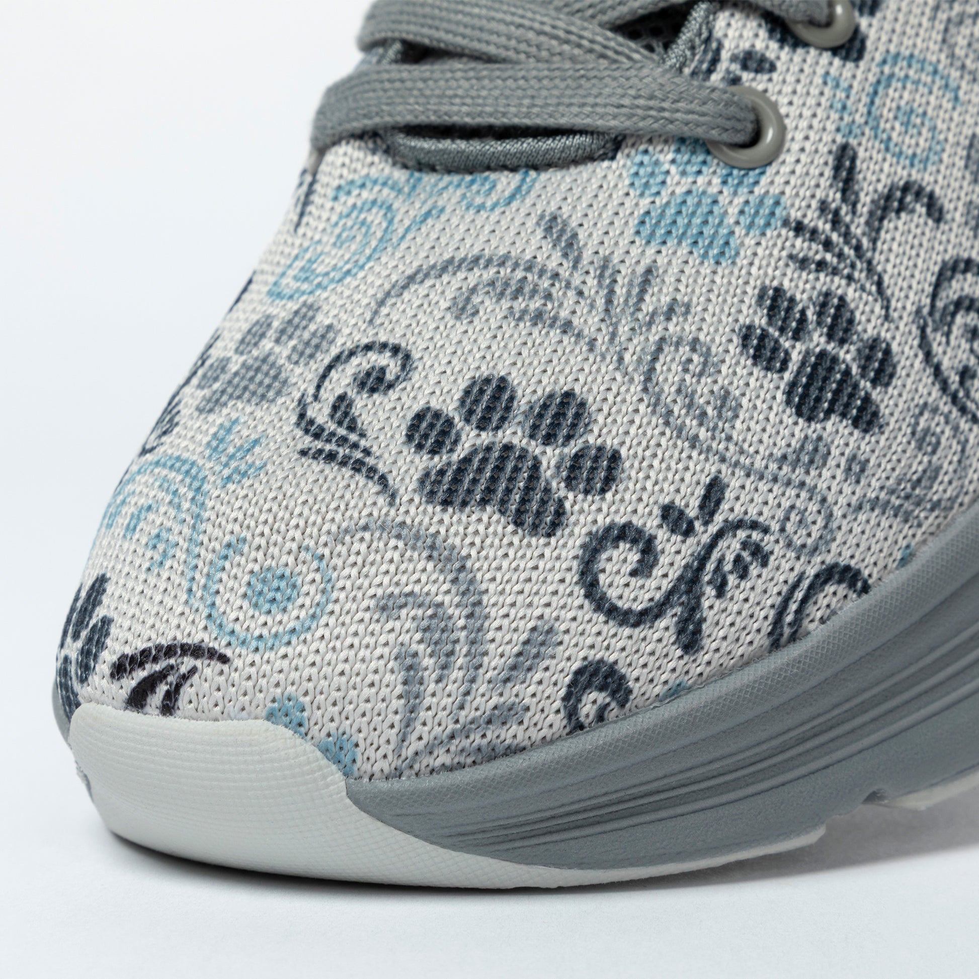 Close-up of a sneaker with a paw print and floral pattern and gray sole on a light background.