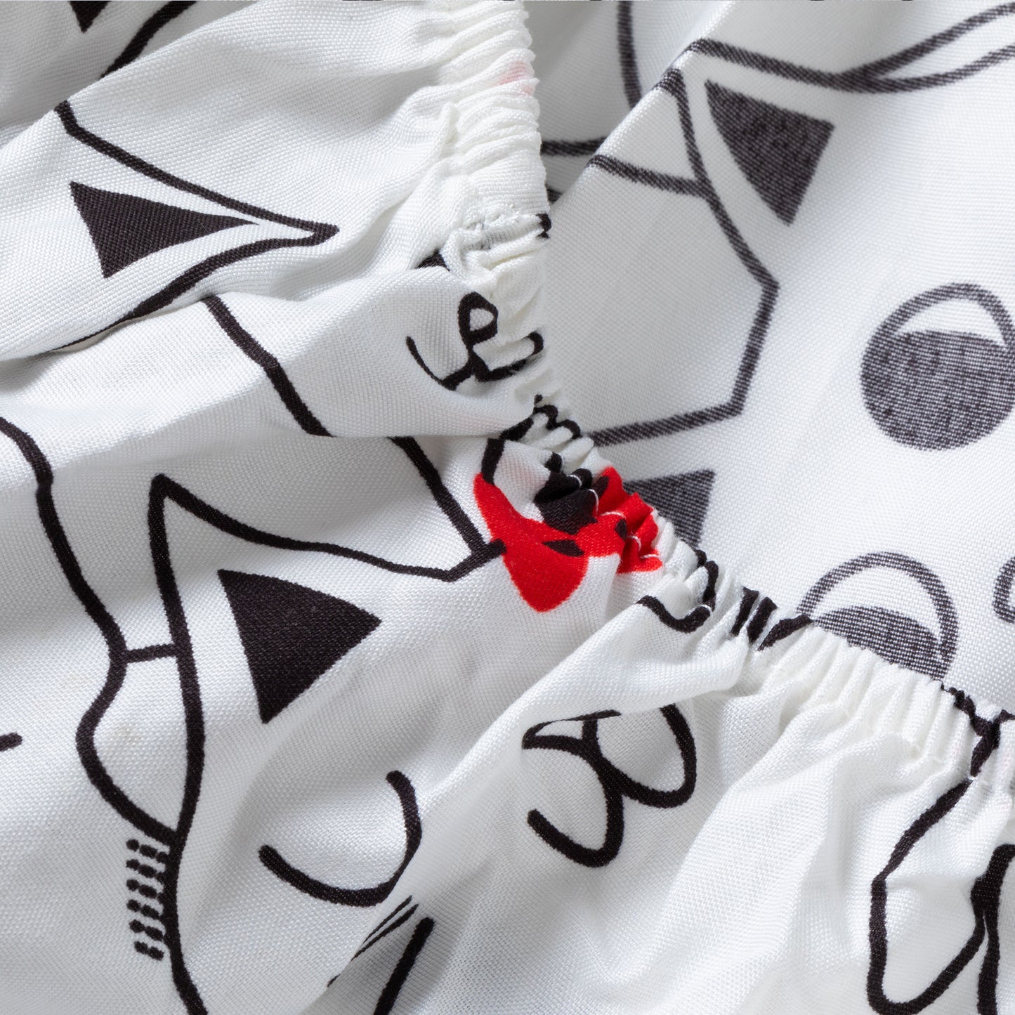 Close-up of a white sheets with a black cat-face line pattern and a small red bow detail near the elasticized waist.
