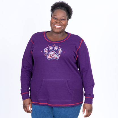 Woman wearing a purple thermal long sleeve top with a kangaroo pocket, and a paisley paw print design on the front, with a white background.