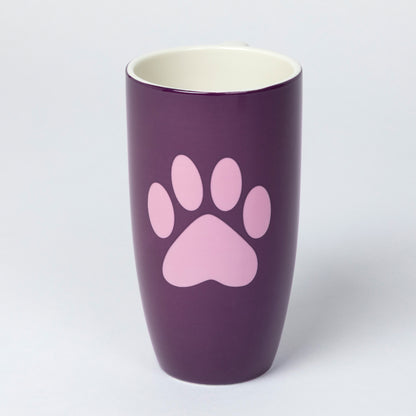A tall, dark purple ceramic mug featuring a light pink paw print graphic on the front, with a cream-colored interior, set against a plain light gray background.