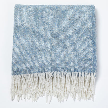 A folded woven throw blanket in a heathered light blue and white colorway, featuring a thick cream-colored fringe along the bottom edge, shown against a plain white background.