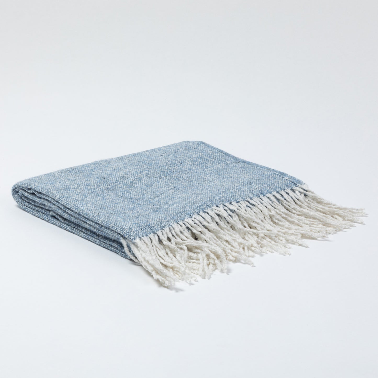 Folded blue blanket with white fringe, resting on a light background.