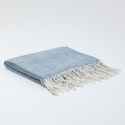 Folded blue blanket with white fringe, resting on a light background.