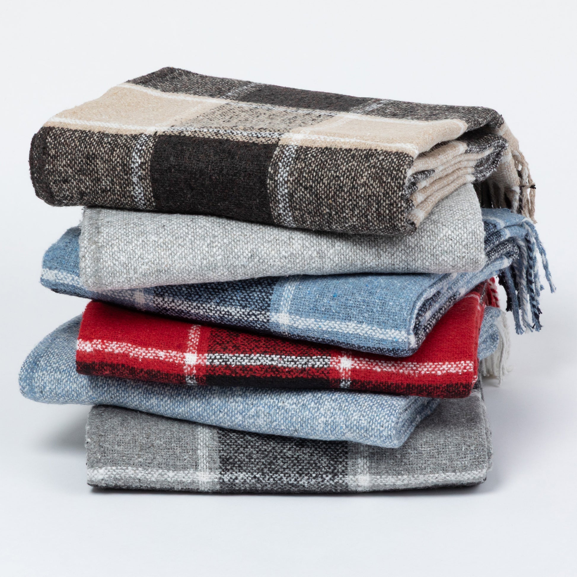 A stack of six folded plaid blankets in various colors and patterns, including black, beige, gray, blue, and red, on a light gray background.
