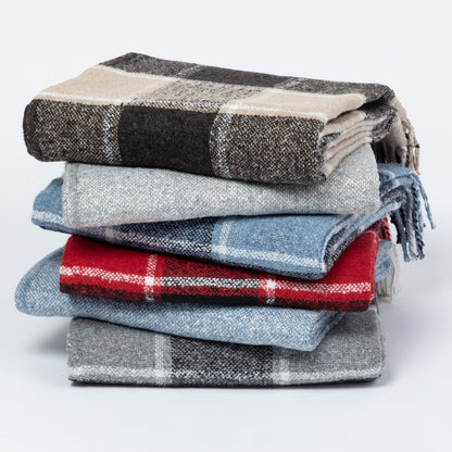 A stack of six folded plaid blankets in various colors and patterns, including black, beige, gray, blue, and red, on a light gray background.