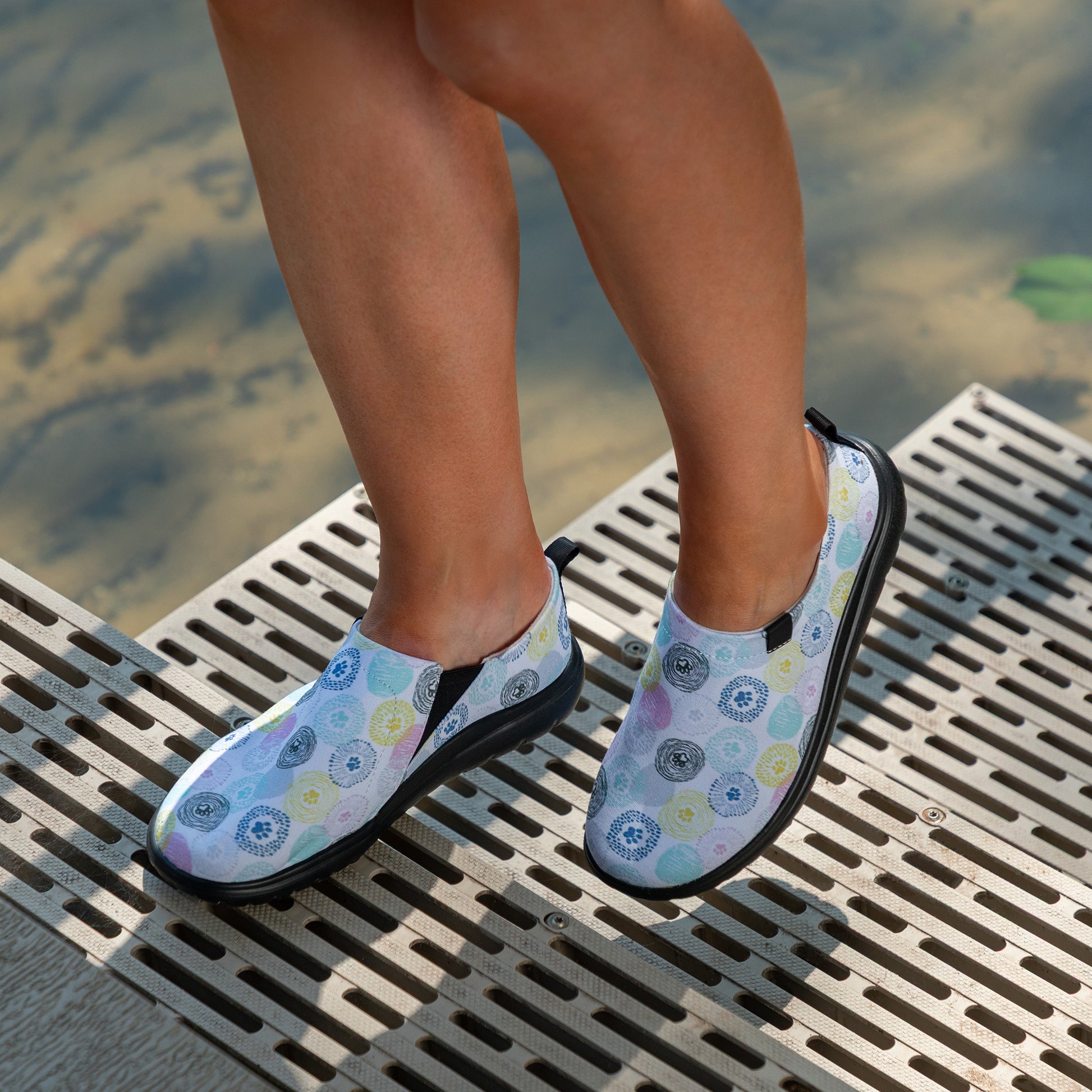 Person wearing patterned shoes standing on a metal platform by water.