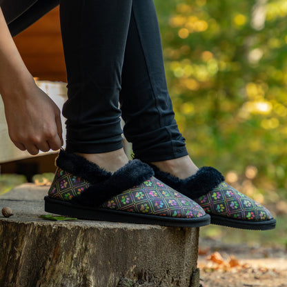 Person wearing black faux fur lined paw printed slipper shoes in outdoor wooded setting.