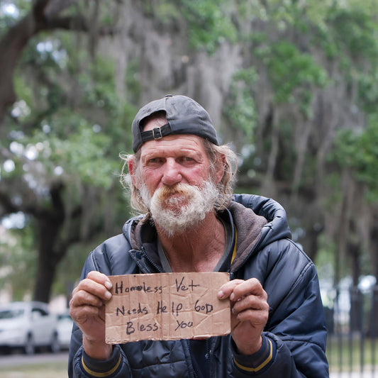 Homeless man holding a sign outdoors with trees in the background
