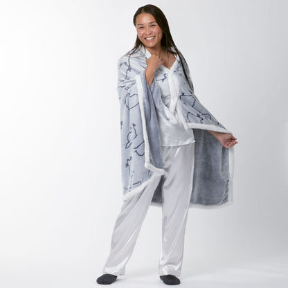 Person wrapped in a gray blanket hoodie with white trim, wearing white pajamas, with a white background.