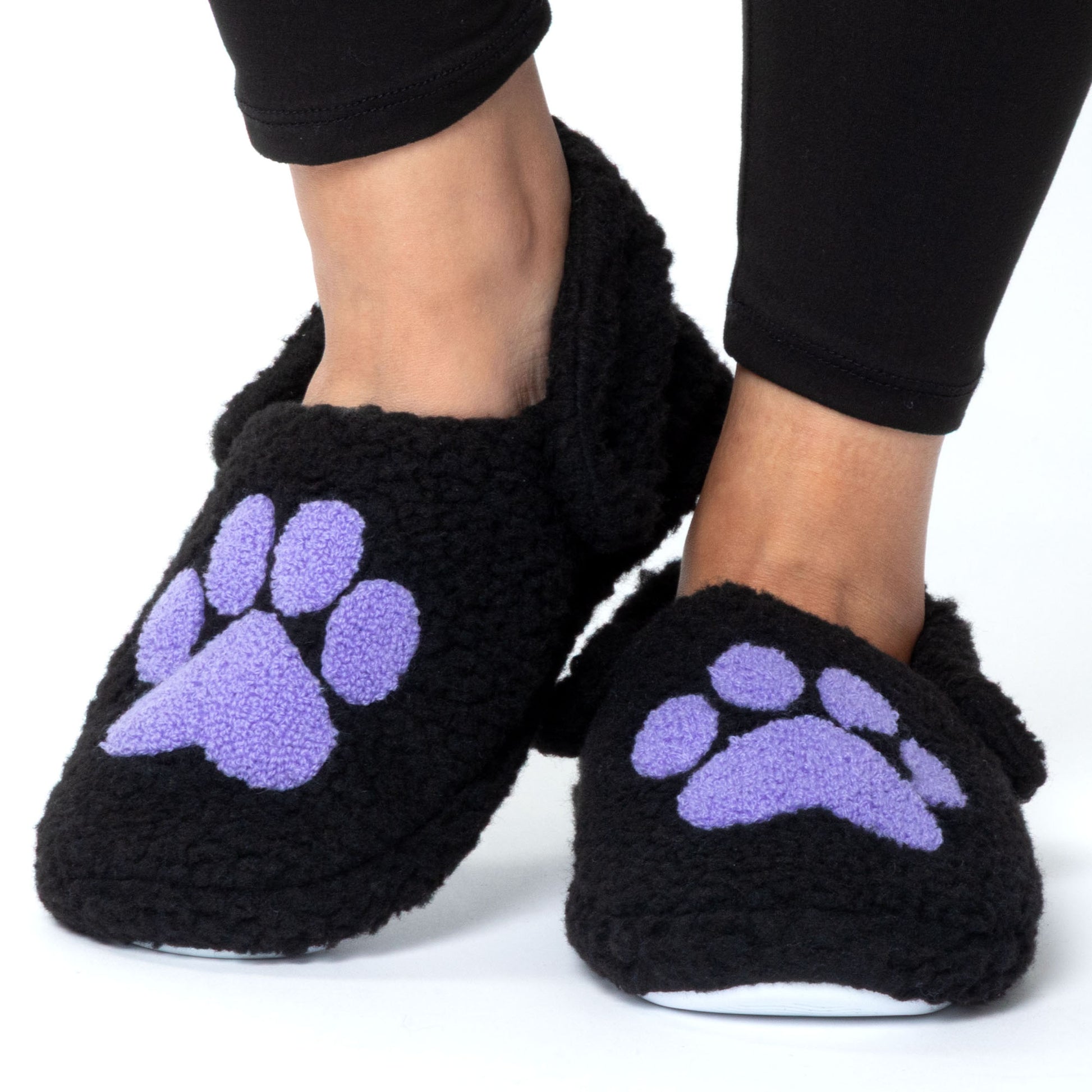 Black slippers with purple paw prints worn by a person on a white background