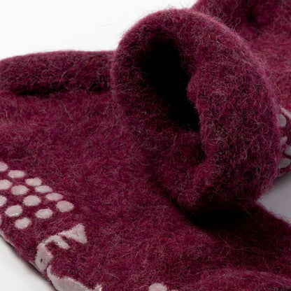 A close-up of a thick, fuzzy felted wool scarf in a deep burgundy color, featuring a white knit pattern along one edge and a rolled cuff showing the soft texture.
